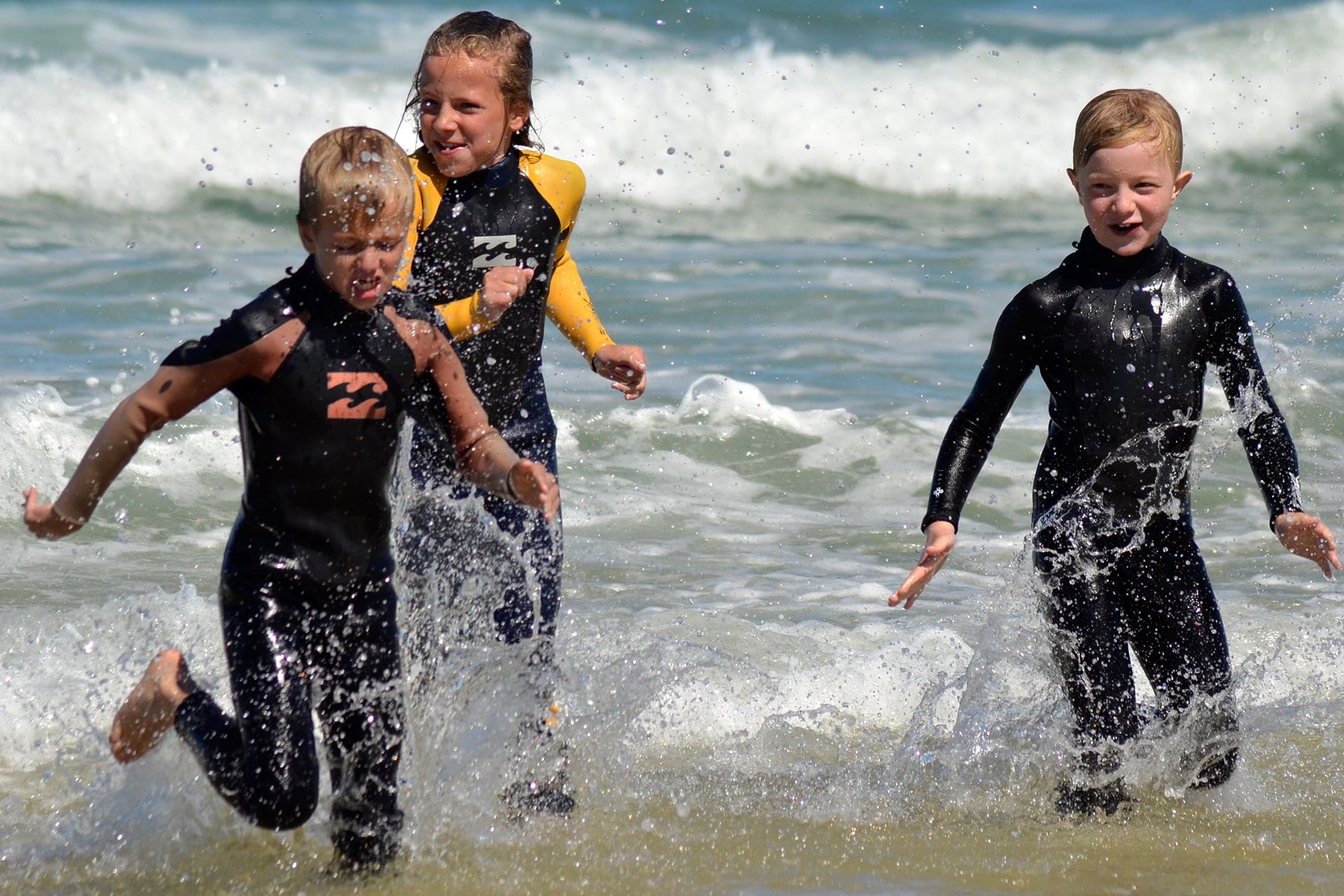 3 jeunes garçons jouant dans les vagues en combinaison néoprène